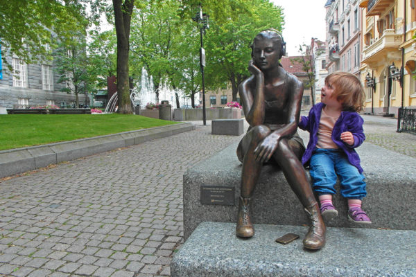 En liten jente sitter ved siden av en statue av en tenåringspike med hodetelefoner.